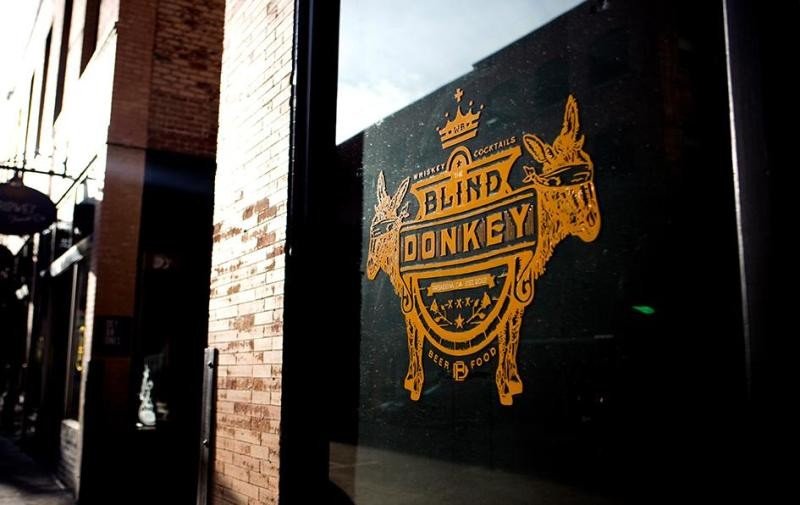 Blind Donkey Pasadena logo painted in orange on a glass window, featuring two donkey silhouettes and decorative lettering
