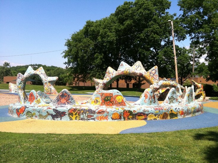 Wide view of the mosaic dragon’s coiled body covered in colorful, hand-placed tiles on a blue and yellow play surface at Dragon Park Nashville