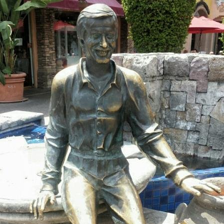 Full-body bronze statue of Sonny Bono seated by a fountain in downtown Palm Springs