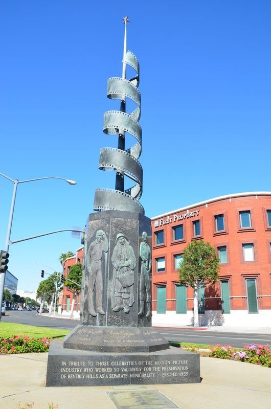 The Celluloid Monument in Beverly Hills—a 22-foot-tall spiraling film-strip sculpture framed by flowers against a clear blue sky