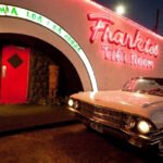 Retro white convertible parked outside the neon-lit entrance of Frankie’s Tiki Room in Las Vegas at night.