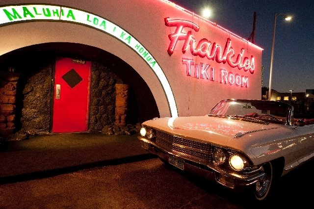 Retro white convertible parked outside the neon-lit entrance of Frankie’s Tiki Room in Las Vegas at night.