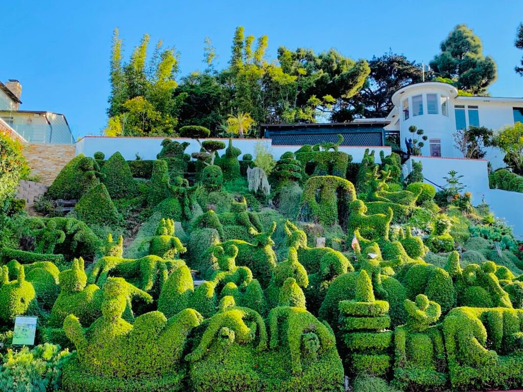 Panoramic hillside of Harper's Topiary Garden in San Diego with dozens of whimsical animal and geometric topiary sculptures beneath a bright blue sky