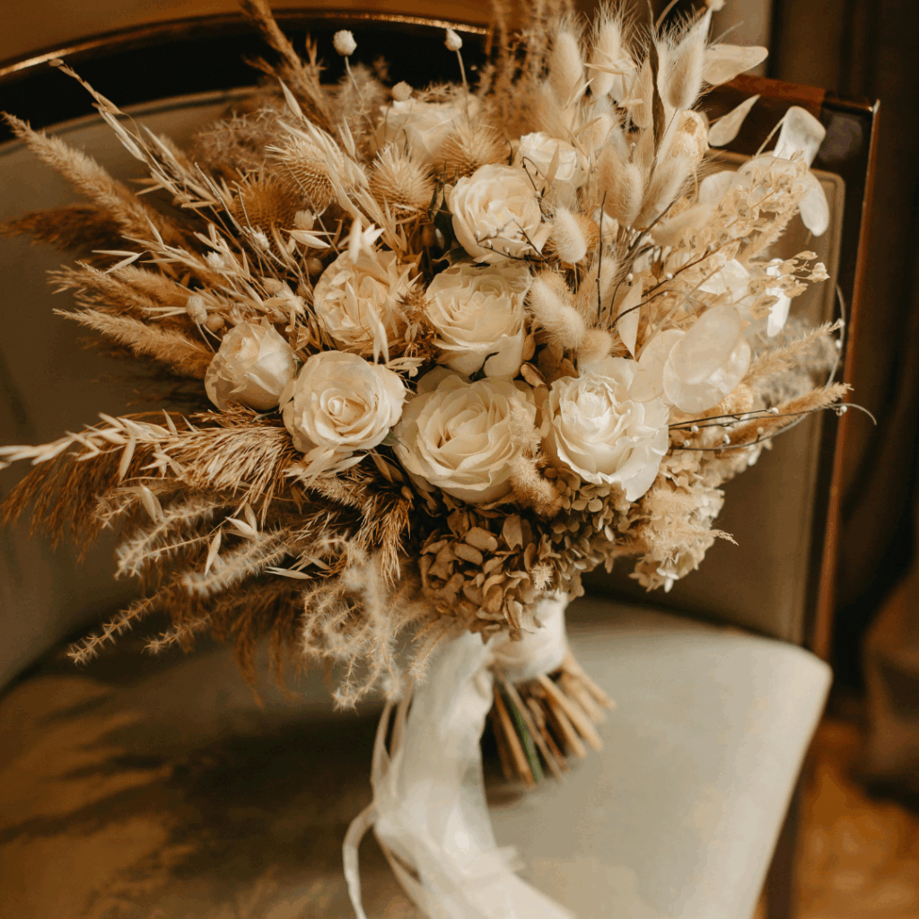 Neutral-toned dried wedding bouquet with white roses, bunny tails, and pampas grass tied with soft ribbon.