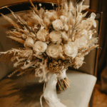 Neutral-toned dried wedding bouquet with white roses, bunny tails, and pampas grass tied with soft ribbon.