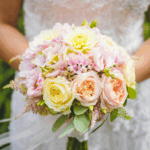 Bride holding a pastel wedding bouquet featuring peach, blush, and cream roses mixed with hydrangeas and greenery.