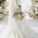 Bride holding bouquet in lace gown during winter wedding prep timeline with floral aisle decor