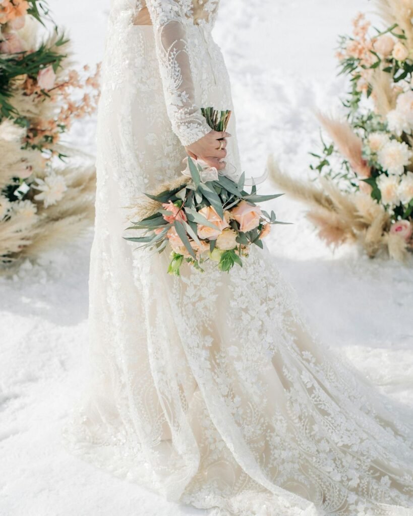 Bride holding bouquet in lace gown during winter wedding prep timeline with floral aisle decor