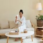 Woman in a white robe applying skincare at home – relaxing setup for a mini spa night in the living room