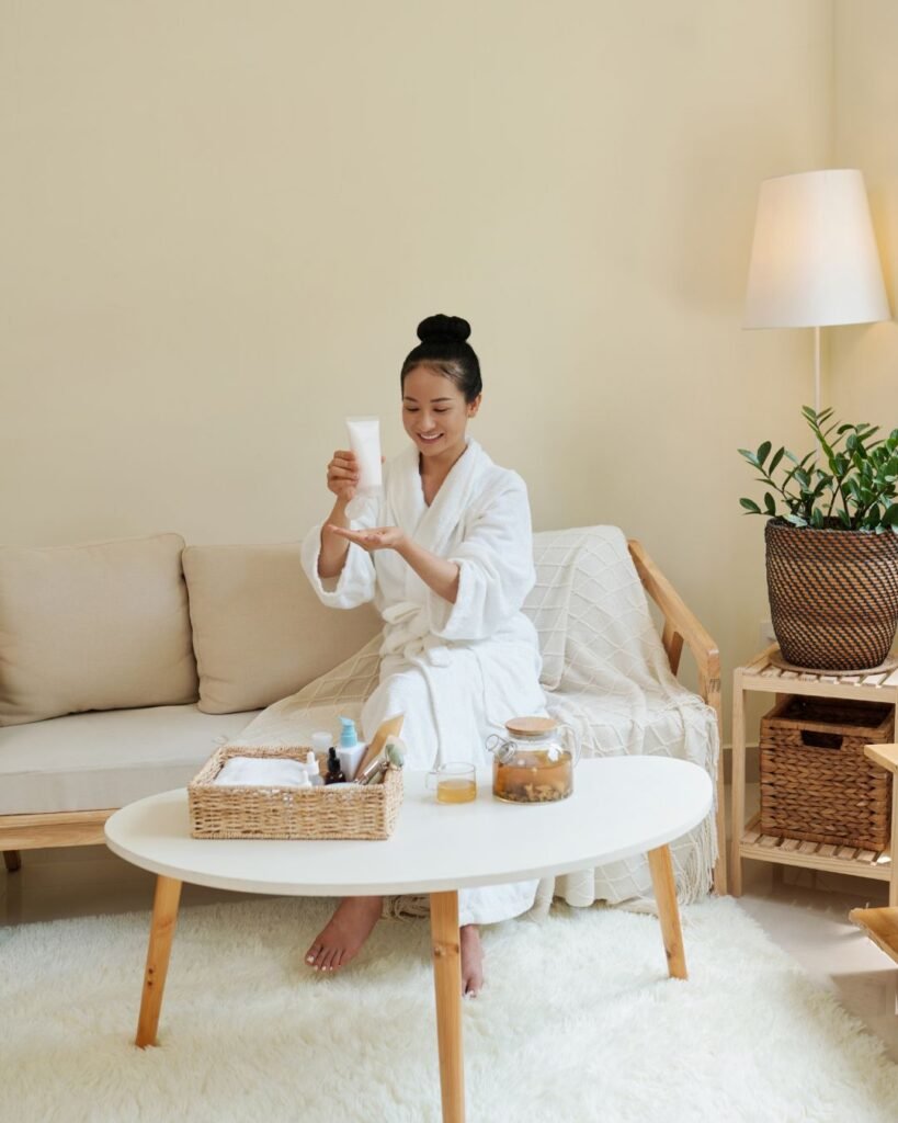 Woman in a white robe applying skincare at home – relaxing setup for a mini spa night in the living room