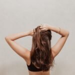 Back view of a woman with natural, mid-length brunette hair wearing a black top and white skirt, posing with hands in her hair—simple vacation hair inspiration.