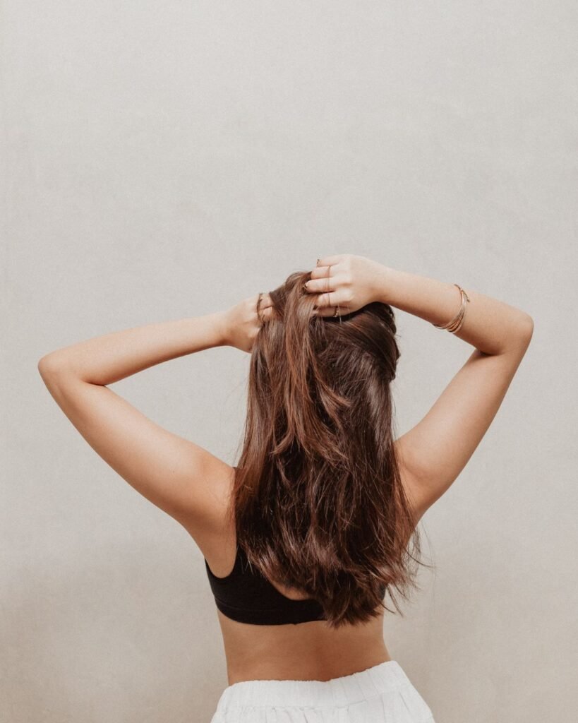 Back view of a woman with natural, mid-length brunette hair wearing a black top and white skirt, posing with hands in her hair—simple vacation hair inspiration.