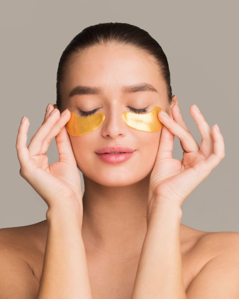 Woman with eyes closed applying gold under eye patches for skincare and puffiness reduction