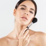 Woman applying makeup with brush – natural dewy skin look for full coverage finish