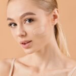 Young woman with flawless skin and two swatches of foundation on cheek, showcasing natural makeup look