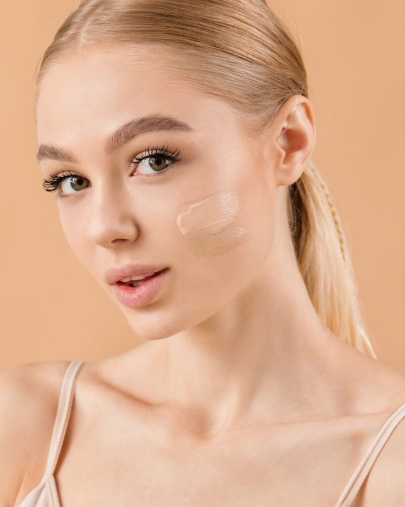 Young woman with flawless skin and two swatches of foundation on cheek, showcasing natural makeup look