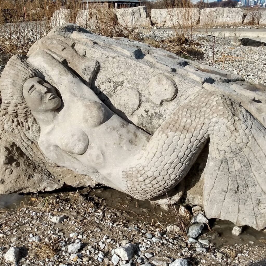 Close-up of the Secret Mermaid Chicago limestone sculpture at Oakwood Beach, showing her scales, tail fin, and serene face