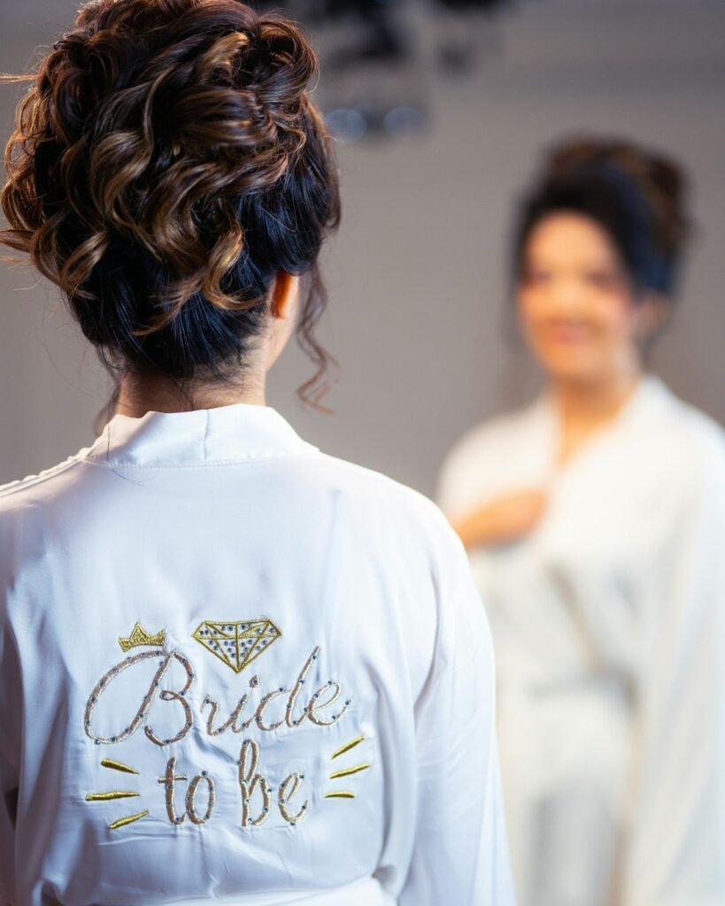 Back view of a personalized bridal robe in white satin embroidered with ‘Bride to Be’ and gold accents