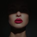 Bold red lipstick to own the night on a woman’s lips bathed in dramatic shadow.