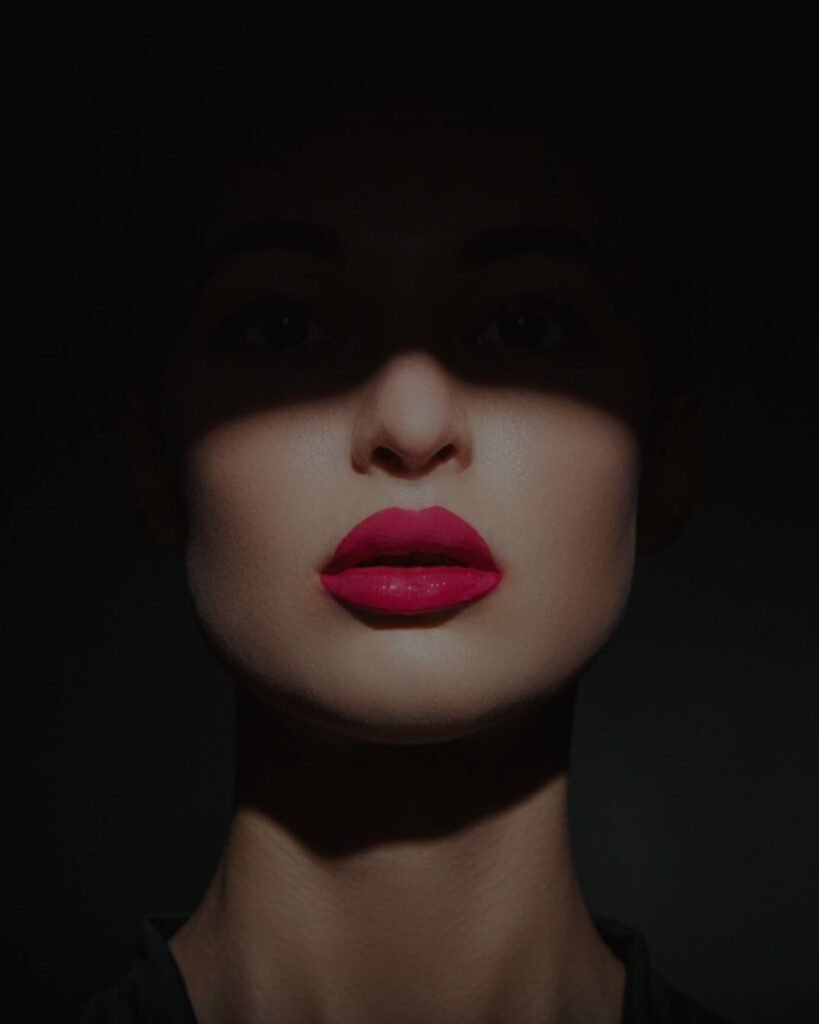 Bold red lipstick to own the night on a woman’s lips bathed in dramatic shadow.