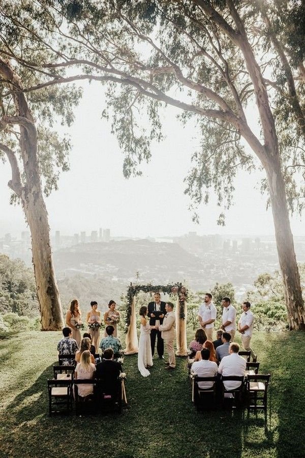 Outdoor micro wedding ceremony under tall trees with city view in the background.