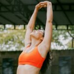 Woman stretching arms overhead in bright orange workout clothes during outdoor exercise