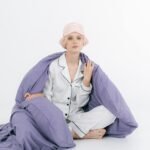 Woman wearing cozy white loungewear pajamas with a lavender blanket and pink sleep mask