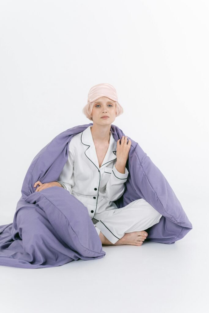 Woman wearing cozy white loungewear pajamas with a lavender blanket and pink sleep mask