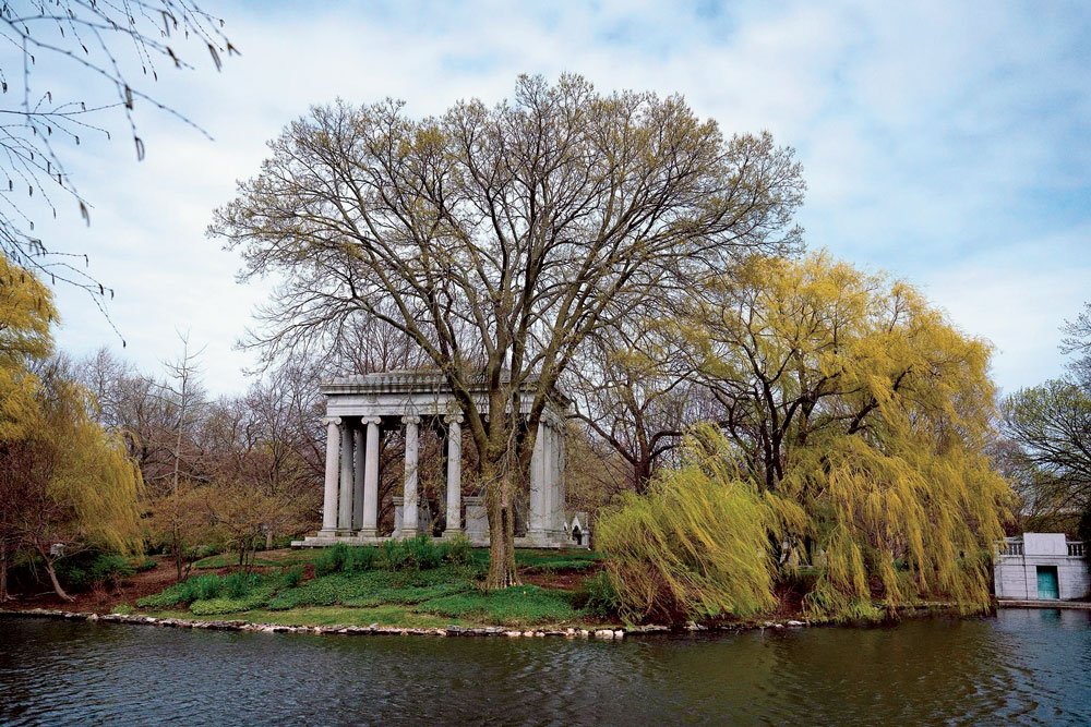 Historic mausoleum surrounded by trees at Graceland Cemetery in Chicago, Illinois, beside a peaceful lake.