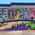 Colorful Phoenix mural featuring bold lettering, a green classic car, city skyline, and cultural street art details in Oak Street Alley, Phoenix, Arizona.