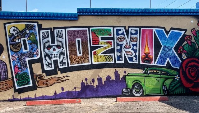 Colorful Phoenix mural featuring bold lettering, a green classic car, city skyline, and cultural street art details in Oak Street Alley, Phoenix, Arizona.