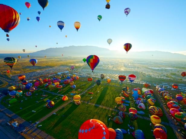 Colorful hot air balloons rising together over a wide desert field near Phoenix, Arizona at sunrise.