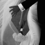 Bride and groom holding hands with white roses in elegant black and white wedding photo.