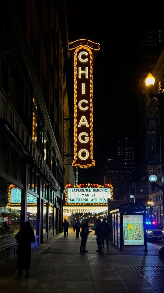 The iconic Chicago Theatre sign illuminated at night with people walking along the street.