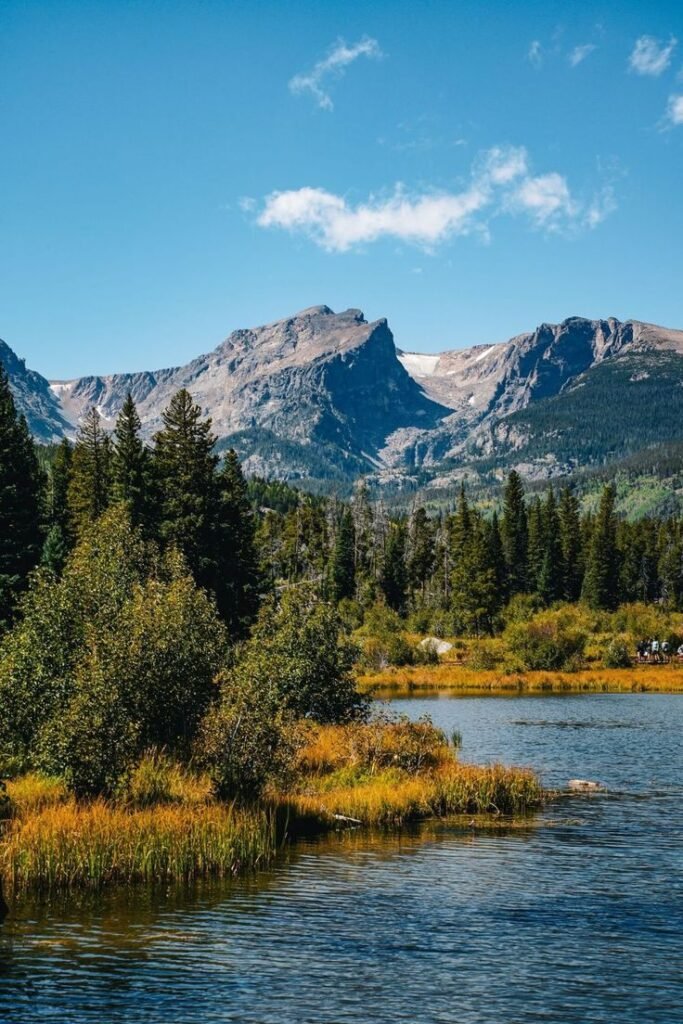 Scenic mountain view at Rocky Mountain National Park near Denver, Colorado, showing alpine peaks, lake reflections, and lush fall foliage.