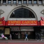 Entrance of Empire Garden Restaurant Boston in Chinatown with red sign and people walking by.