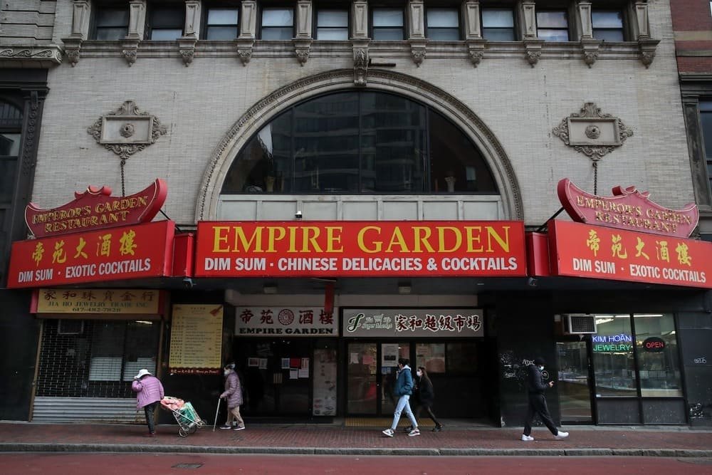 Entrance of Empire Garden Restaurant Boston in Chinatown with red sign and people walking by.