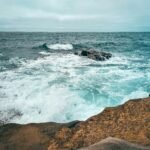 Waves crashing against coastal rocks in San Diego on a cloudy day, showcasing the natural beauty of the Pacific Ocean.