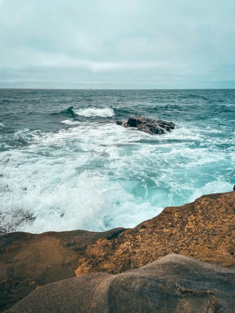 Waves crashing against coastal rocks in San Diego on a cloudy day, showcasing the natural beauty of the Pacific Ocean.