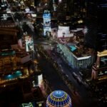 Aerial night view of the Las Vegas Strip featuring bright neon signs, hotels, and busy streets below.