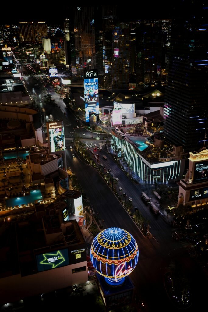 Aerial night view of the Las Vegas Strip featuring bright neon signs, hotels, and busy streets below.
