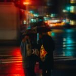 Two friends walking under umbrellas during an evening rain in New York City
