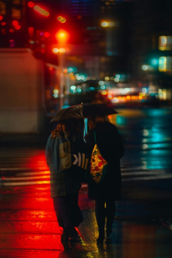 Two friends walking under umbrellas during an evening rain in New York City