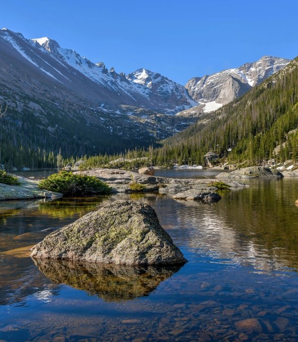 Scenic alpine lake in Rocky Mountain National Park with snow-capped peaks and pine trees near Denver, Colorado.
