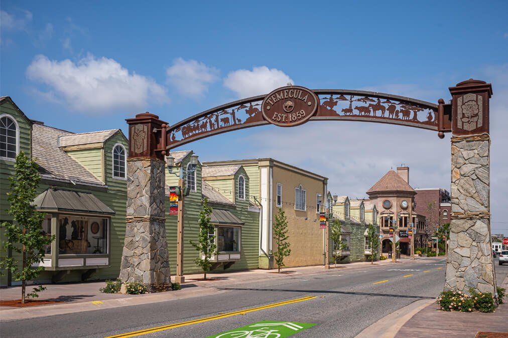 Historic Temecula arch sign at the entrance of Old Town Temecula with colorful buildings and clear blue sky.